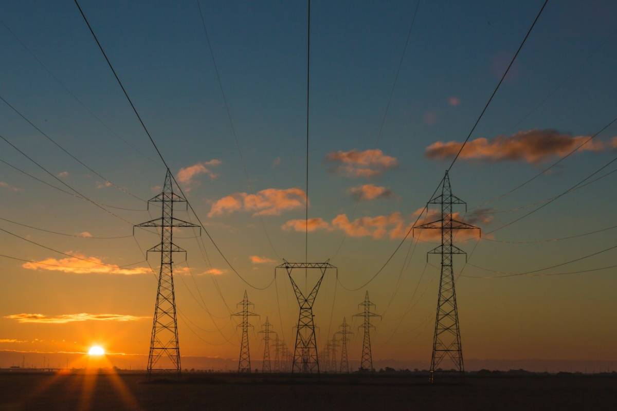 High-voltage transmission towers marching toward a setting sun